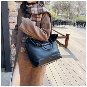 Close-up of black leather tote bag with unique woven handles and wide nylon shoulder strap
