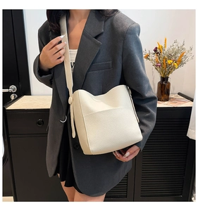 Close-up of a white leather bucket bag with wide strap worn by a model in suit