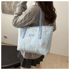 Détail d'un grand cabas bleu clair avec broderie ondulée colorée et plaque de marque chic