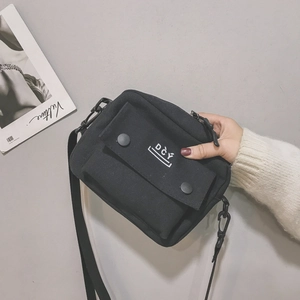 Detail of black canvas messenger bag featuring a front flap pocket with two buttons and DCY logo