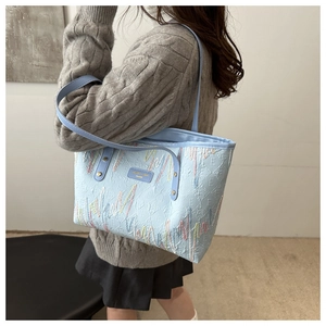 Détail du sac cabas rayé bleu clair avec broderie coeur et plaque logo métallique