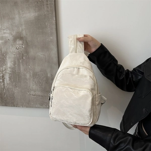 Minimalist beige multi-pocket crossbody sling bag with textured fabric and zipper details
