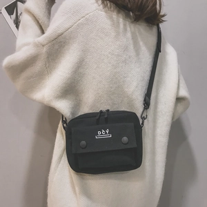 Detail of a black canvas crossbody bag featuring a front pocket with white DCY logo