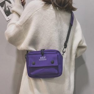 Detail of purple canvas crossbody bag with letter print and metal buckles on a model