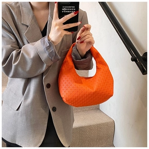 Detail of a bright orange woven hobo bag with a seamless handle and textured geometric pattern