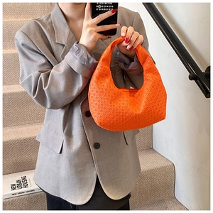 Detail of vibrant orange woven crescent bag held by a model in a grey casual suit