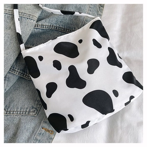 Détail d'un sac cabas en toile à motif vache posé sur un drap blanc avec veste en jean
