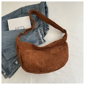 Detail of a brown corduroy crossbody bag with adjustable strap over a denim jacket