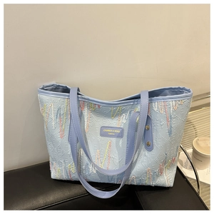 Détail du sac cabas bleu clair avec coutures ondulées colorées et étiquette en cuir