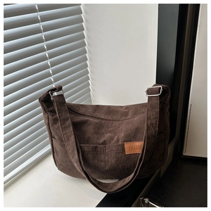 Detail of dark brown corduroy crossbody bag featuring adjustable strap and fashion label