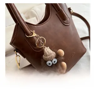 Detail of brown textured leather bucket bag with a funny plush monster charm and gold buckle