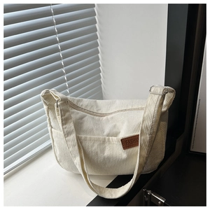 Close-up of beige corduroy tote bag featuring a leather fashion label and adjustable strap