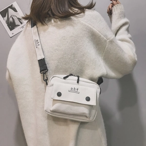 Detail of off-white canvas crossbody bag featuring black DCY lettering and wide strap