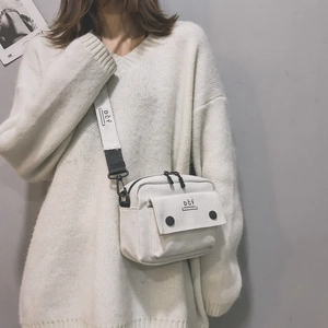 Detail of white canvas crossbody bag featuring DCY logo strap and black buckle closure