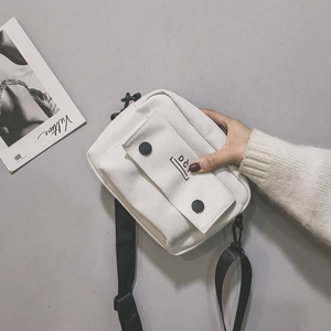 Detail view of a white canvas crossbody bag featuring a front pocket and adjustable strap
