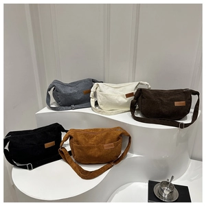Five corduroy crossbody bags in various colors with adjustable straps on a display stand