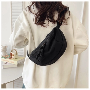 Detail view of black canvas crescent chest bag with woven rope zipper pulls on white hoodie