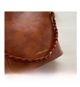 Gros plan du sac seau en cuir vintage marron avec bandoulière tressée et logo doré