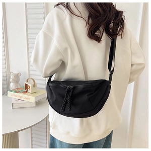 Detail of black crescent crossbody bag with woven zipper pullers on a model