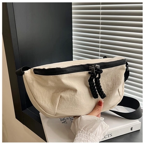 Detail of minimalist cream crossbody bag featuring black zipper and woven rope pullers
