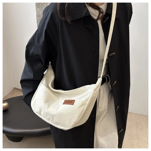 Detailed shot of white corduroy crescent bag with adjustable strap and leather logo patch