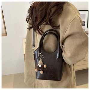 Deep brown bucket bag with a cute plush charm shown on model in a minimalist setting
