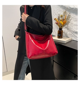Detail of a large red glossy leather tote bag shown on a model with a black wool coat