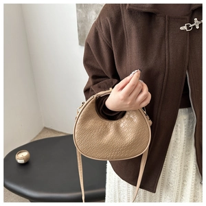 Detail shot of a khaki crescent bag with woven texture worn with a brown coat