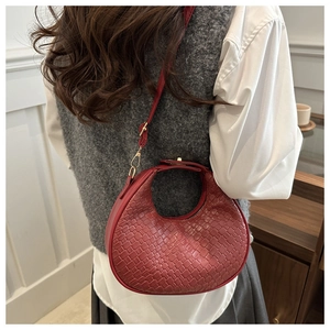 Detail of red woven crescent bag with gold hardware worn on a shoulder strap