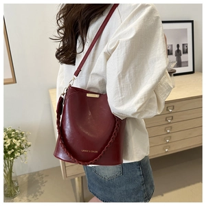 Détail d'un sac seau bordeaux vintage avec poignée tressée et marquage doré élégant