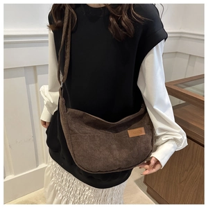 Close-up of brown corduroy crossbody bag featuring a fashion leather label and textured fabric