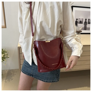 Détail du sac seau bordeaux avec poignée tressée et pièce décorative en métal doré