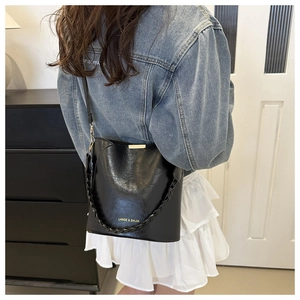 Modèle portant un sac seau noir brillant avec poignée tressée et logo doré discret