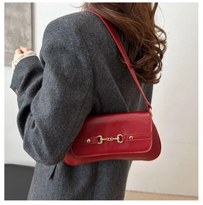 Detail of red faux leather shoulder bag with golden horsebit metal hardware on flap