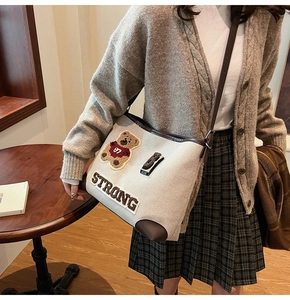 Detail view of beige canvas tote bag featuring bear embroidery and brown leather trim