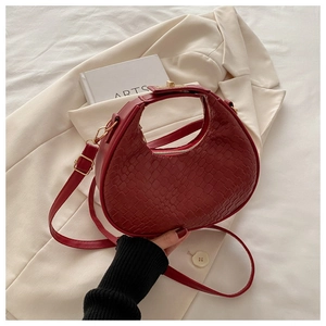 Detail of red faux crocodile leather texture and gold buckle on a stylish crescent bag