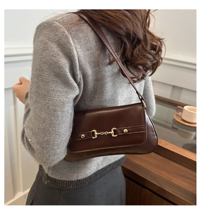 Close-up of vintage brown shoulder bag featuring a gold horsebit buckle on artificial leather