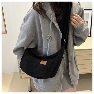 Detail of black corduroy crossbody crescent bag featuring a brown fashion leather patch
