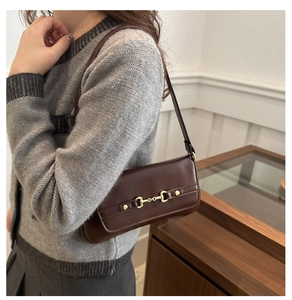 Detail of dark brown polished leather shoulder bag with golden horsebit hardware buckle