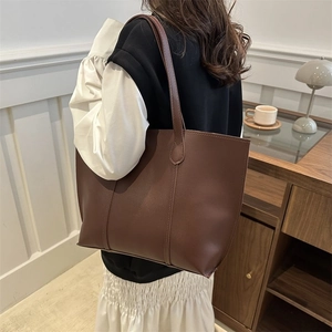 Detail view of large brown PU leather tote bag with shoulder strap worn by a model