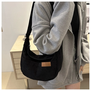 Close-up of black corduroy crescent bag with a leather label on a shoulder strap