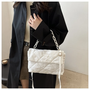 Détail d'un sac bandoulière blanc matelassé avec boucle dorée et chaîne sur manteau noir