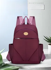 Detailed close-up of water-resistant burgundy nylon backpack with golden logo