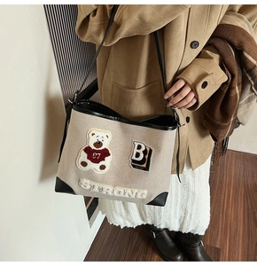 Detail view of canvas tote bag featuring embroidered bear patch and faux leather trim