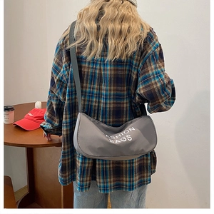 Detail view of gray nylon crescent crossbody bag with large FASHION BAGS printed text