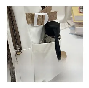 Detail of off-white backpack side pocket holding a black folding umbrella and strap