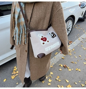 Close-up of beige canvas tote with teddy bear embroidery and brown leather trim details