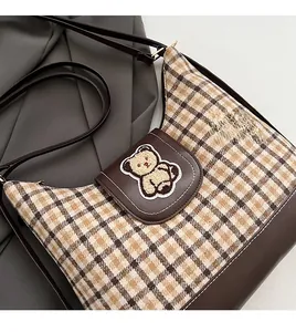 Detailed view of checkered canvas tote bag with brown leather flap and plush bear patch