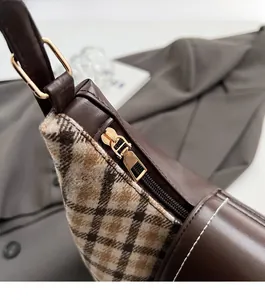 Close-up of smooth gold metal zipper and brown plaid fabric stitching on tote bag