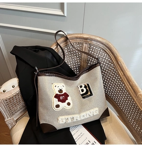 Close-up of retro canvas tote bag with plush bear patch and leather shoulder strap